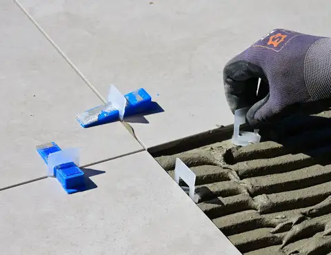 Gloved hand placing a tile leveling spacer over fresh mortar during floor tile installation